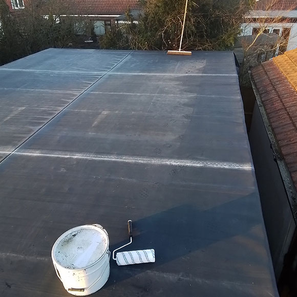 a complete flat roof with a bucket of sealant and broom on top